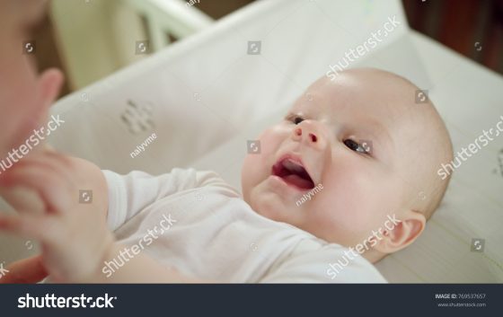 stock-photo-baby-s-smiling-lying-in-bed-on-white-linen-and-playning-with-its-mother-close-up-shot-769537657